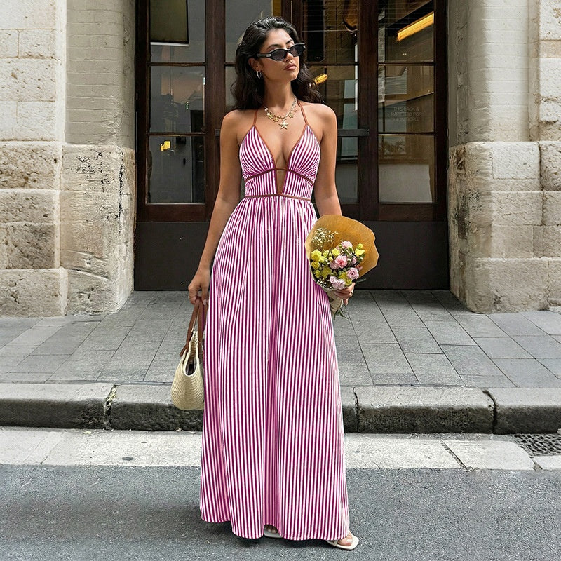 Woman in a pink striped dress holding flowers and a yellow bag on a city street.