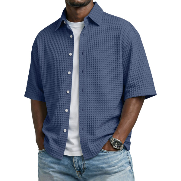 Man wearing a blue textured shirt over a white shirt with jeans on a white background