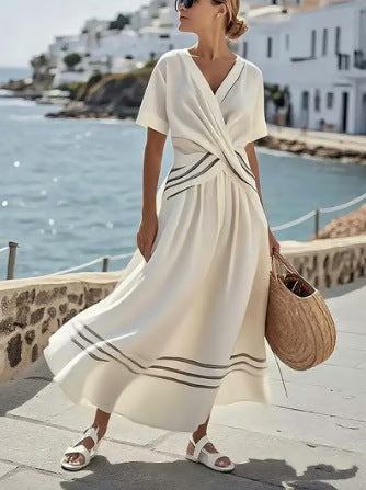 Woman in a white dress with black stripes standing by a scenic coastal area.