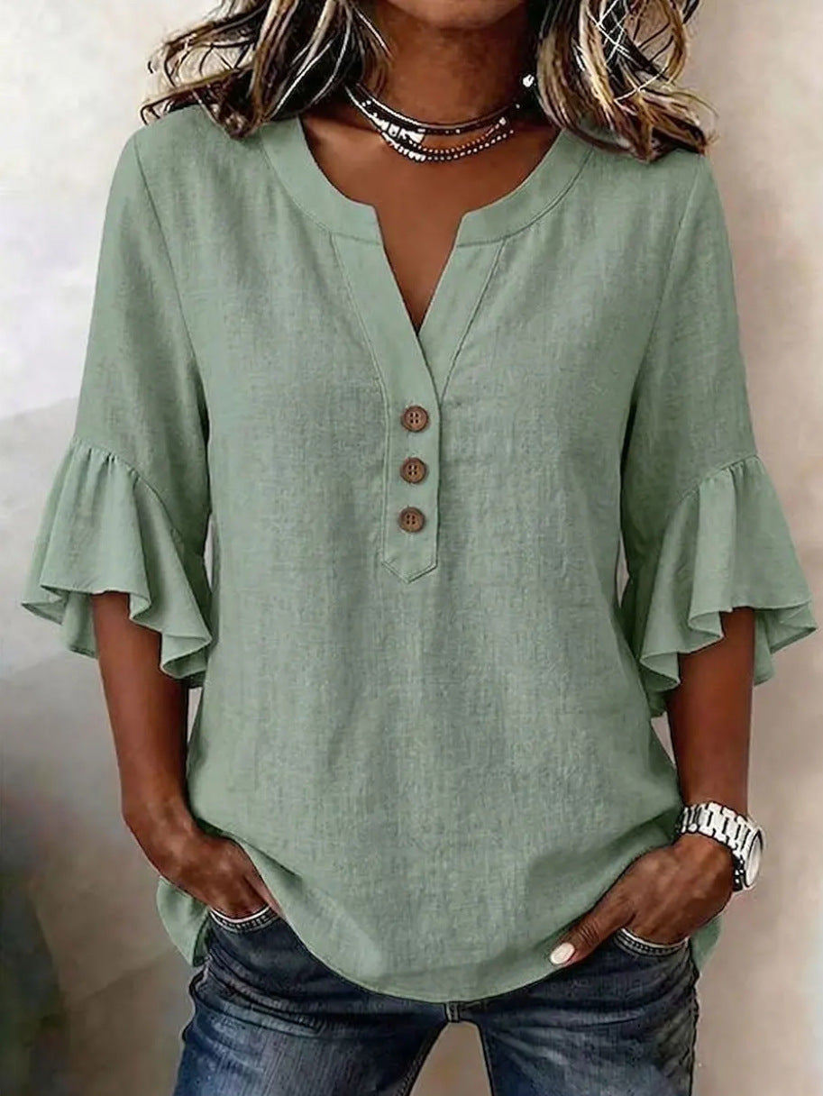Person wearing a green blouse with ruffled sleeves and blue jeans against a neutral background