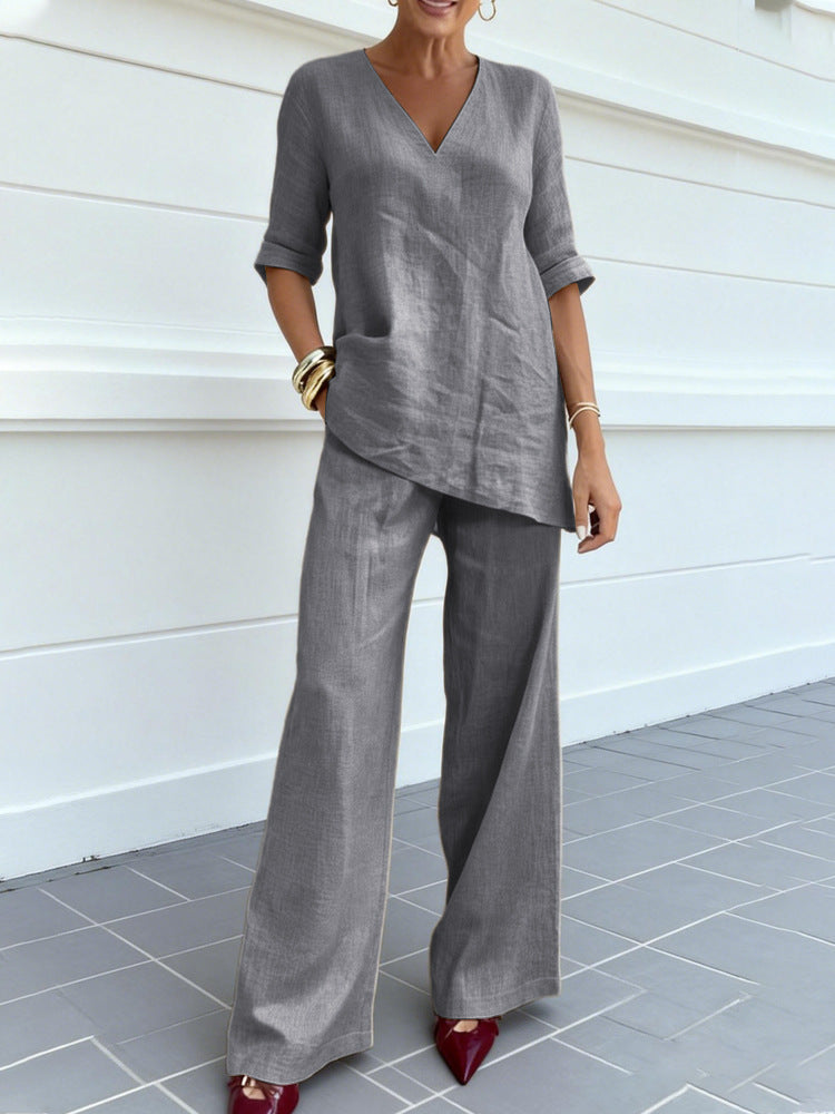 Person wearing a gray outfit with wide-leg pants against a white wall.