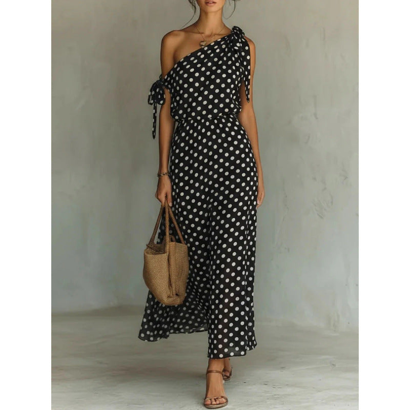 Woman wearing a black and white polka dot dress holding a woven bag against a plain background