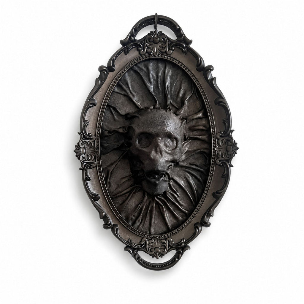 An ornate oval gothic wall plaque featuring a dark metallic relief sculpture of a skull with sunburst rays and a ruffled collar, set against a plain white background.