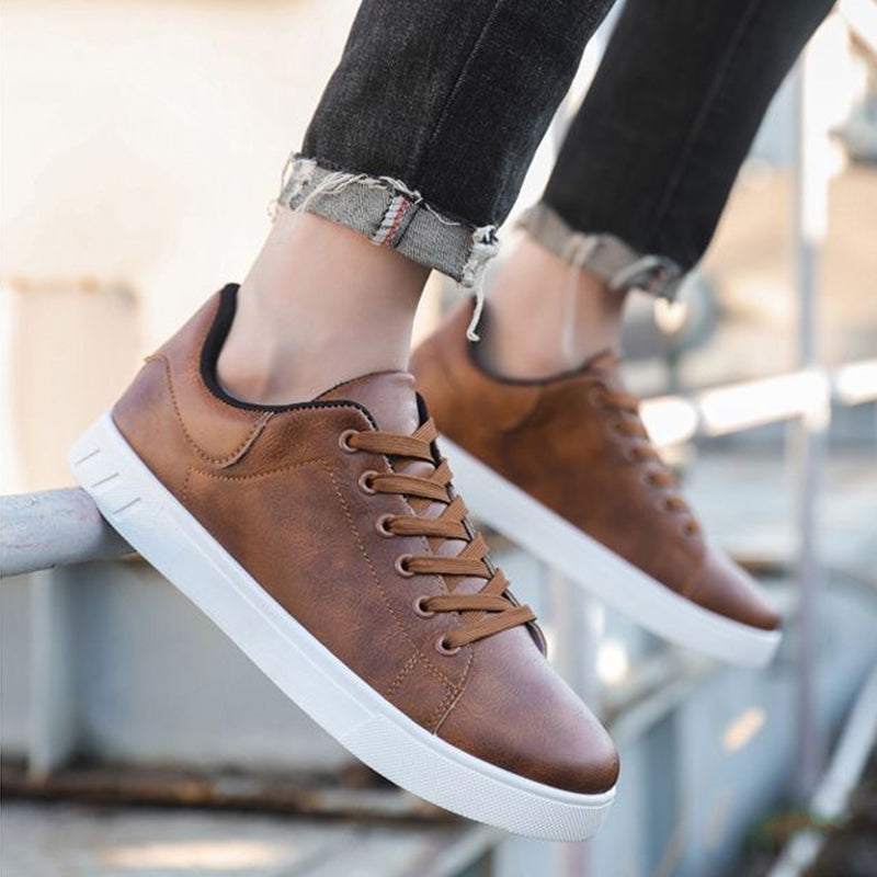 Brown sneakers with white soles worn by a person sitting on a metal railing.