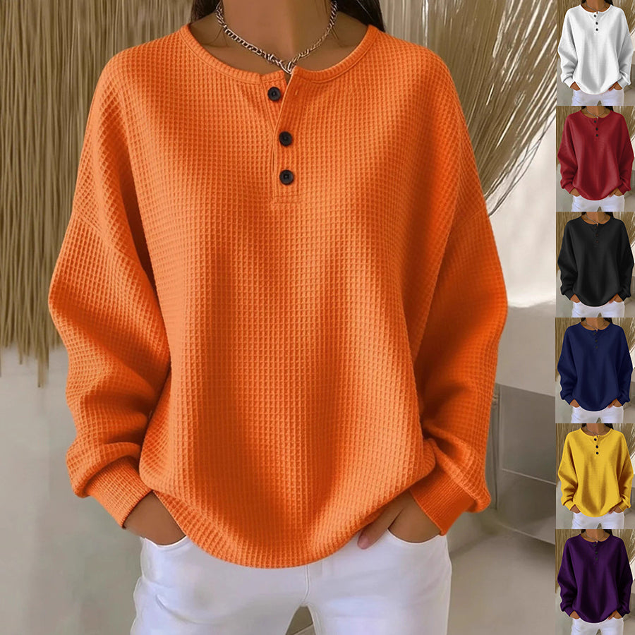 A woman wearing a bright orange waffle-knit long-sleeve henley top with three dark buttons, shown in a lifestyle-style indoor setting. Along the right side, smaller inset images show the same top in additional colors: white, burgundy, black, gray, navy, yellow, mustard, and purple.