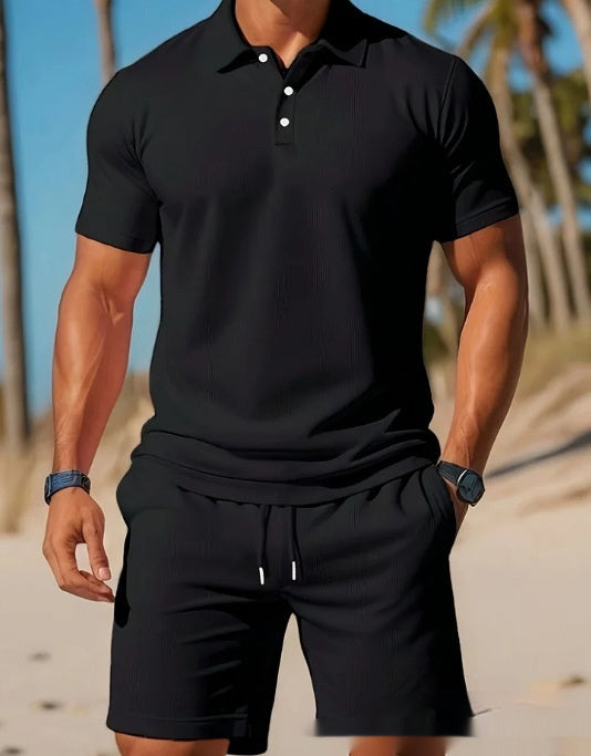 Man wearing a black polo shirt and shorts on a beach.