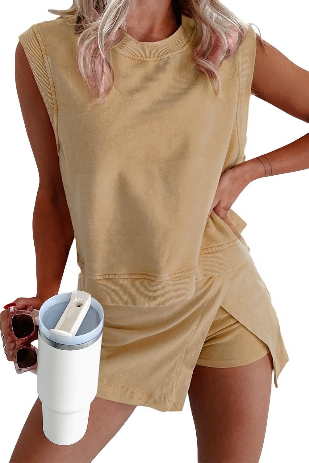 Woman wearing a beige sleeveless top and shorts, holding sunglasses and a white cup with a blue lid.