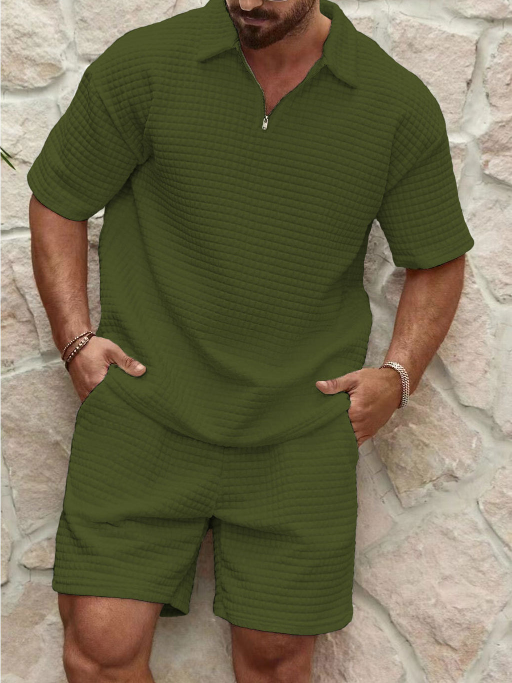Man wearing a green textured polo shirt and shorts set against a stone wall.