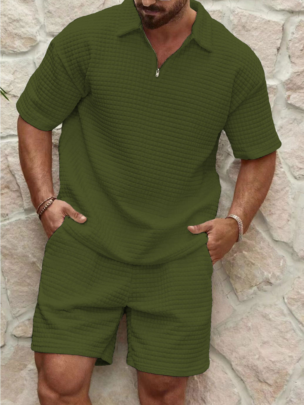 Man wearing a green textured polo shirt and shorts set against a stone wall.