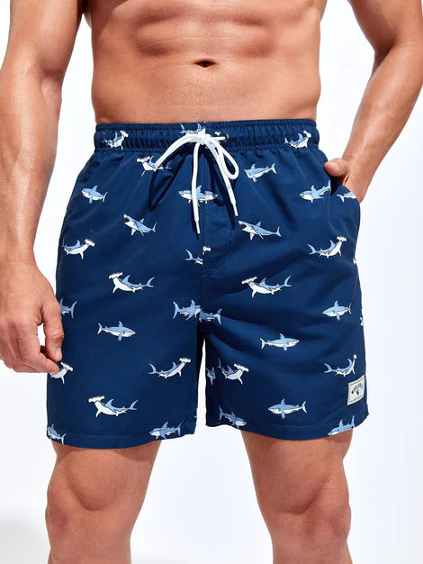 Navy blue swim shorts with shark pattern worn by a person on a white background