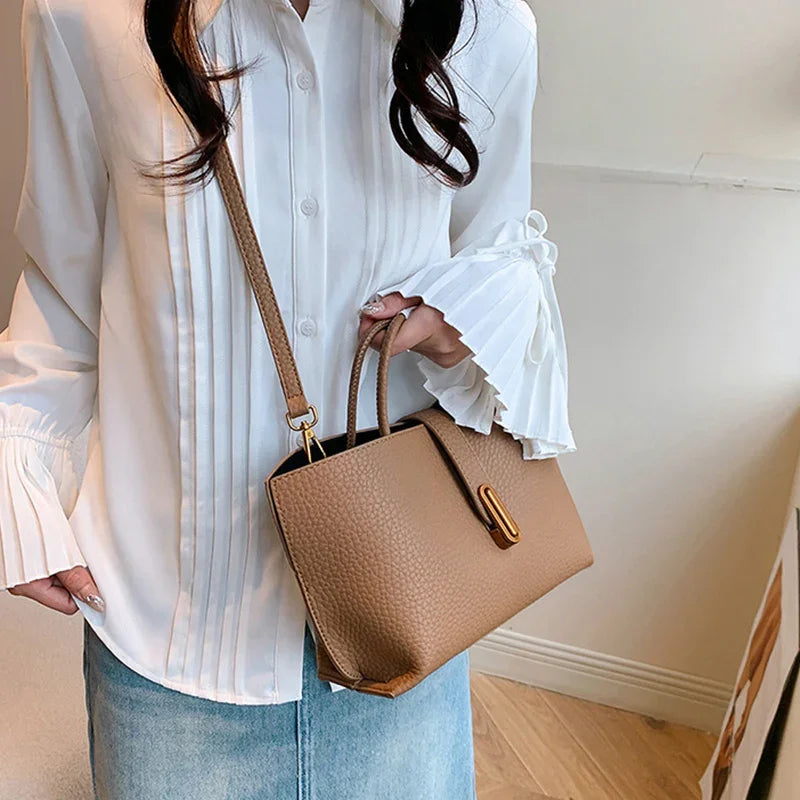 Person holding a brown handbag wearing a white blouse and light blue jeans indoors.