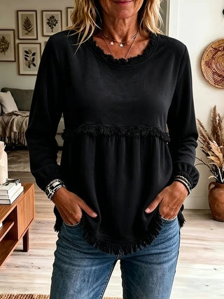 Woman wearing a black long-sleeve top with ruffled details in a living room setting.