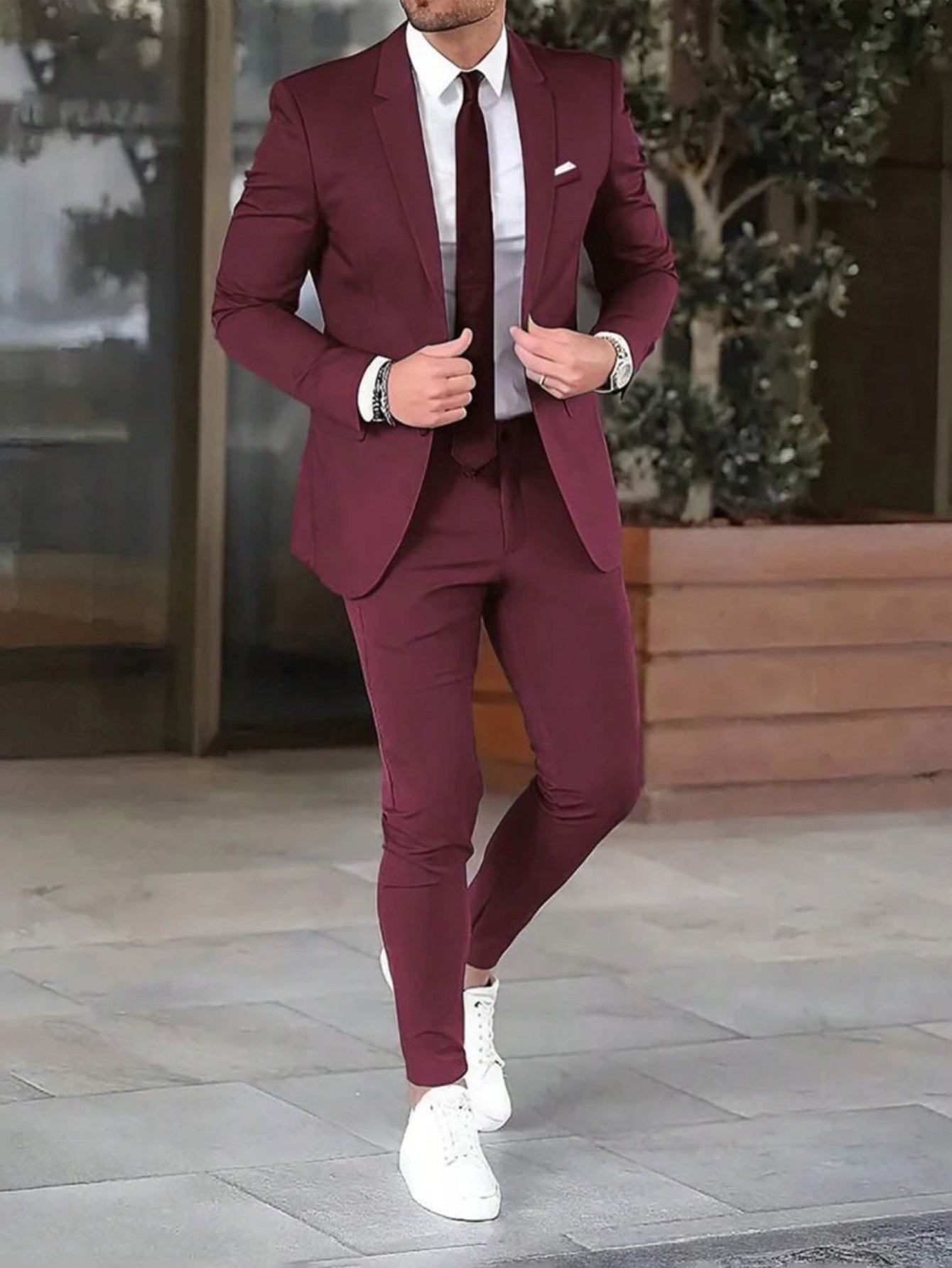 Man wearing a burgundy suit with white shoes on a city street.