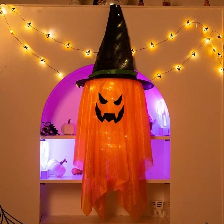 Halloween-themed decoration with a ghost costume and pumpkin face on an archway with string lights.