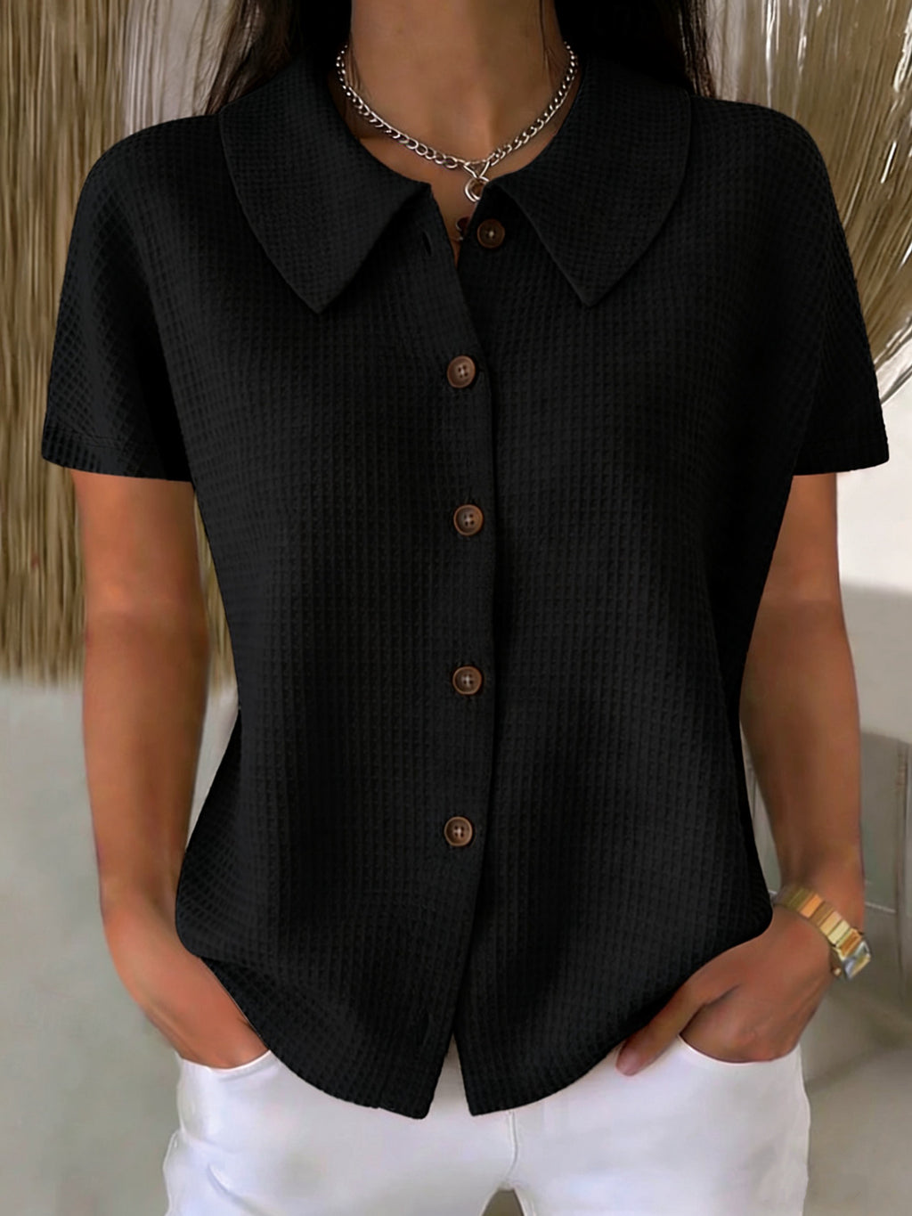 Person wearing a black short-sleeve button-up shirt with a neutral background