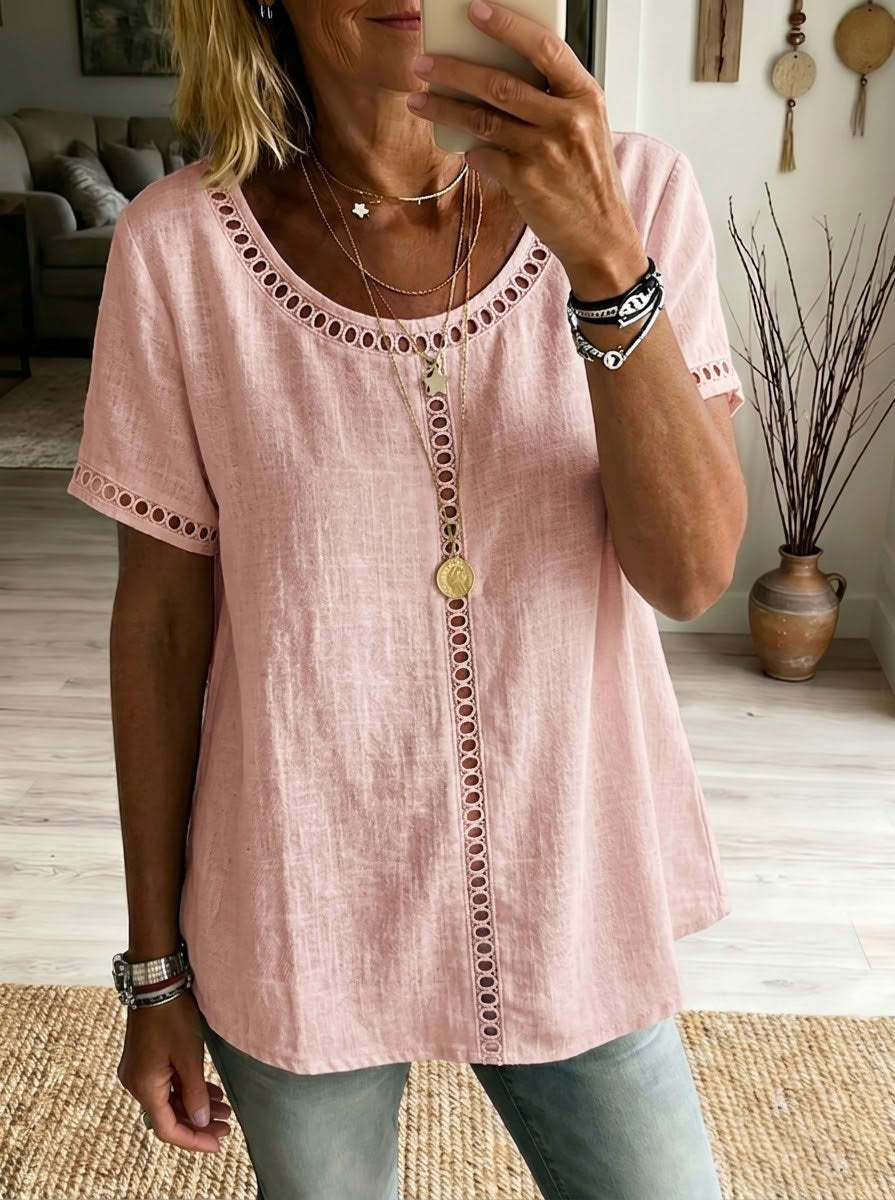 Person wearing a pink blouse with decorative buttons and trim in a home setting.
