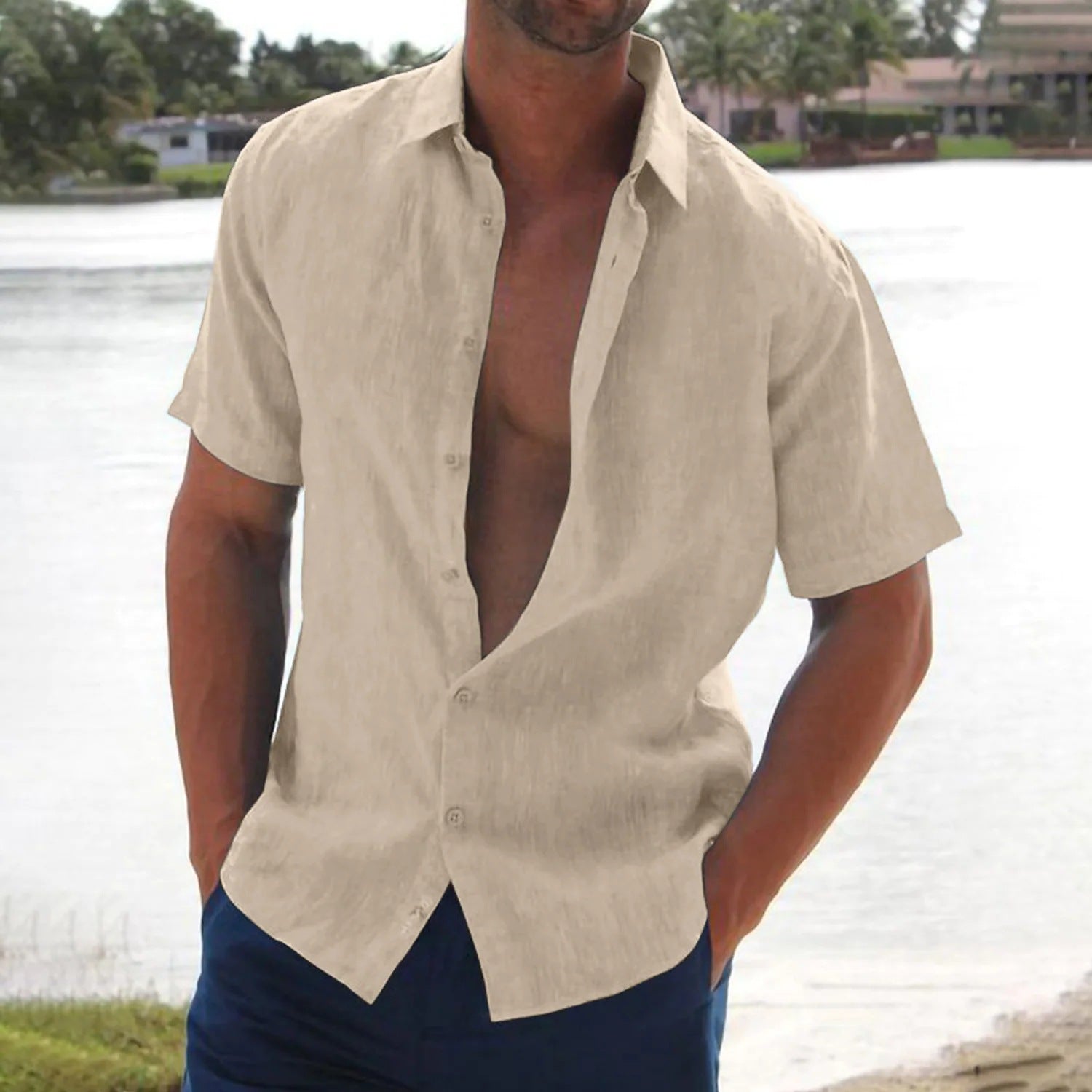 Man wearing a beige linen shirt with short sleeves, standing by a body of water.