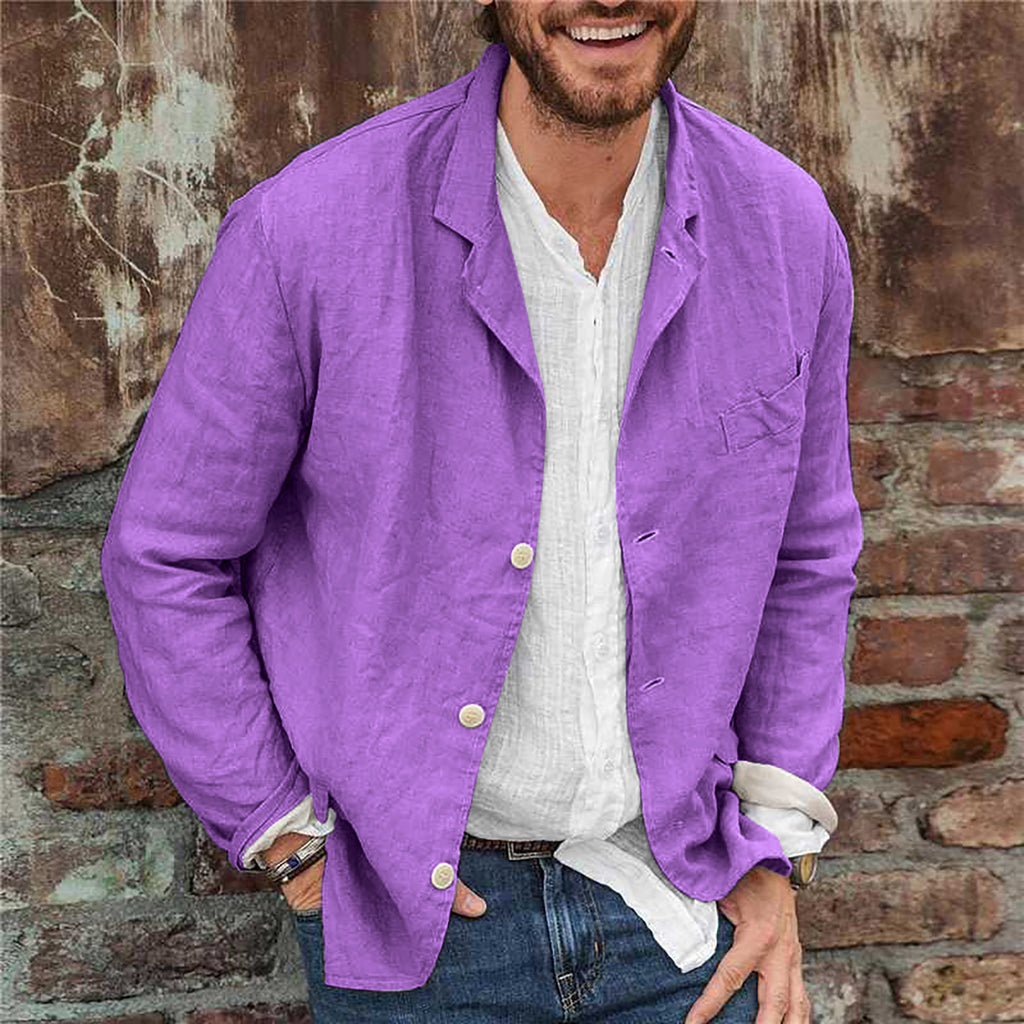 Man wearing a purple jacket over a white shirt, standing against a brick wall.