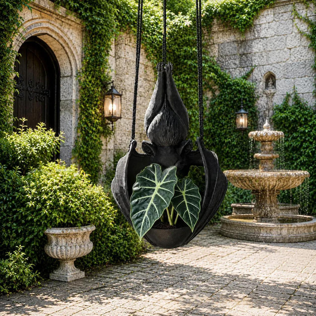 A black hanging planter shaped like a stylized flower or leaf, suspended in a stone courtyard with ivy-covered walls, a fountain, and a potted plant inside.