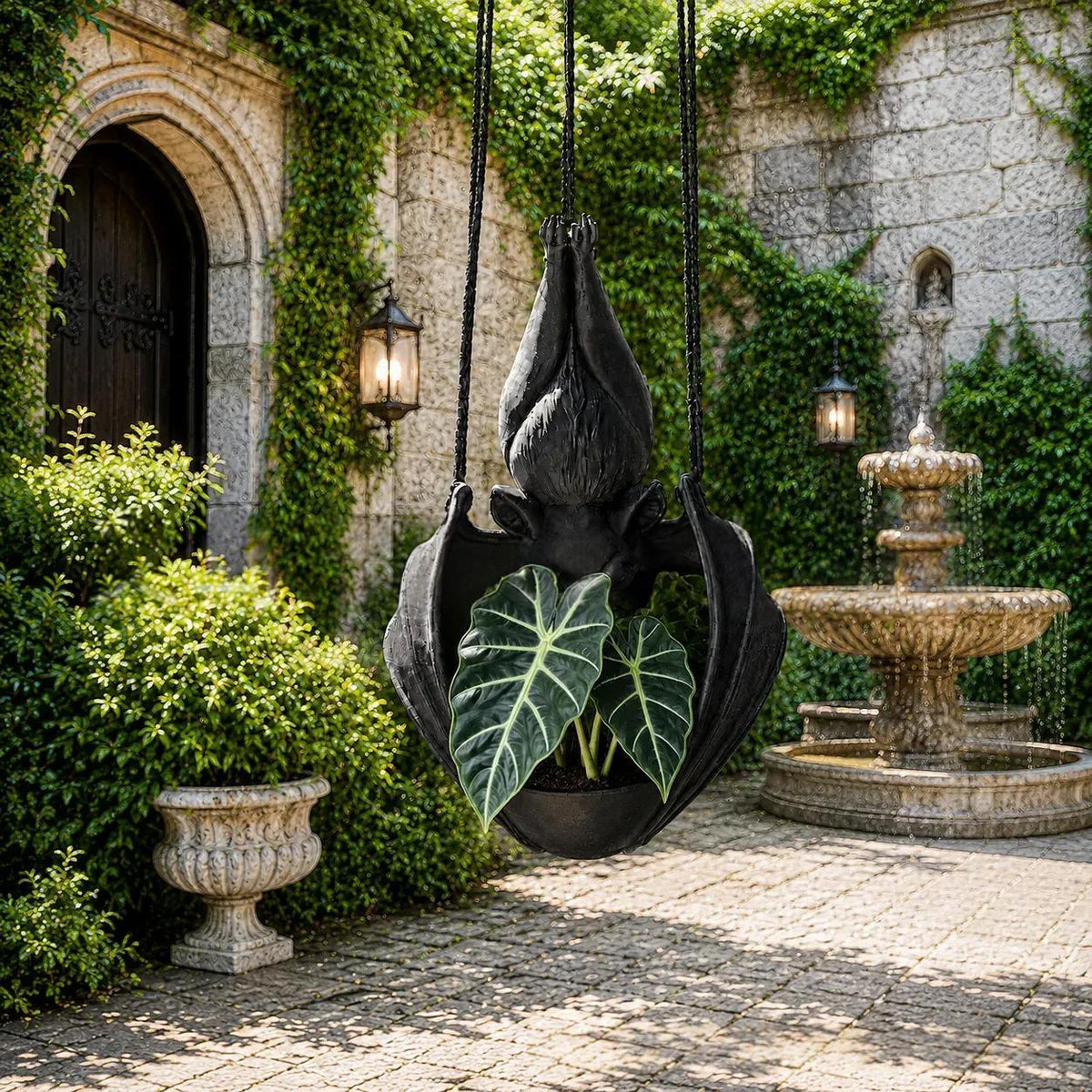 A black hanging planter shaped like a stylized flower or leaf, suspended in a stone courtyard with ivy-covered walls, a fountain, and a potted plant inside.