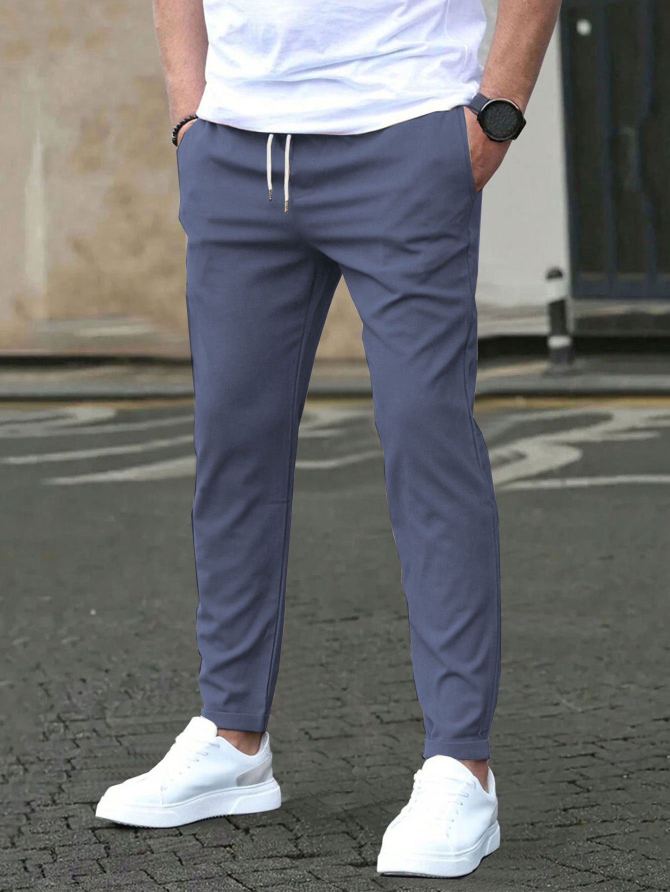 Person wearing blue jogger pants and white sneakers on a street.