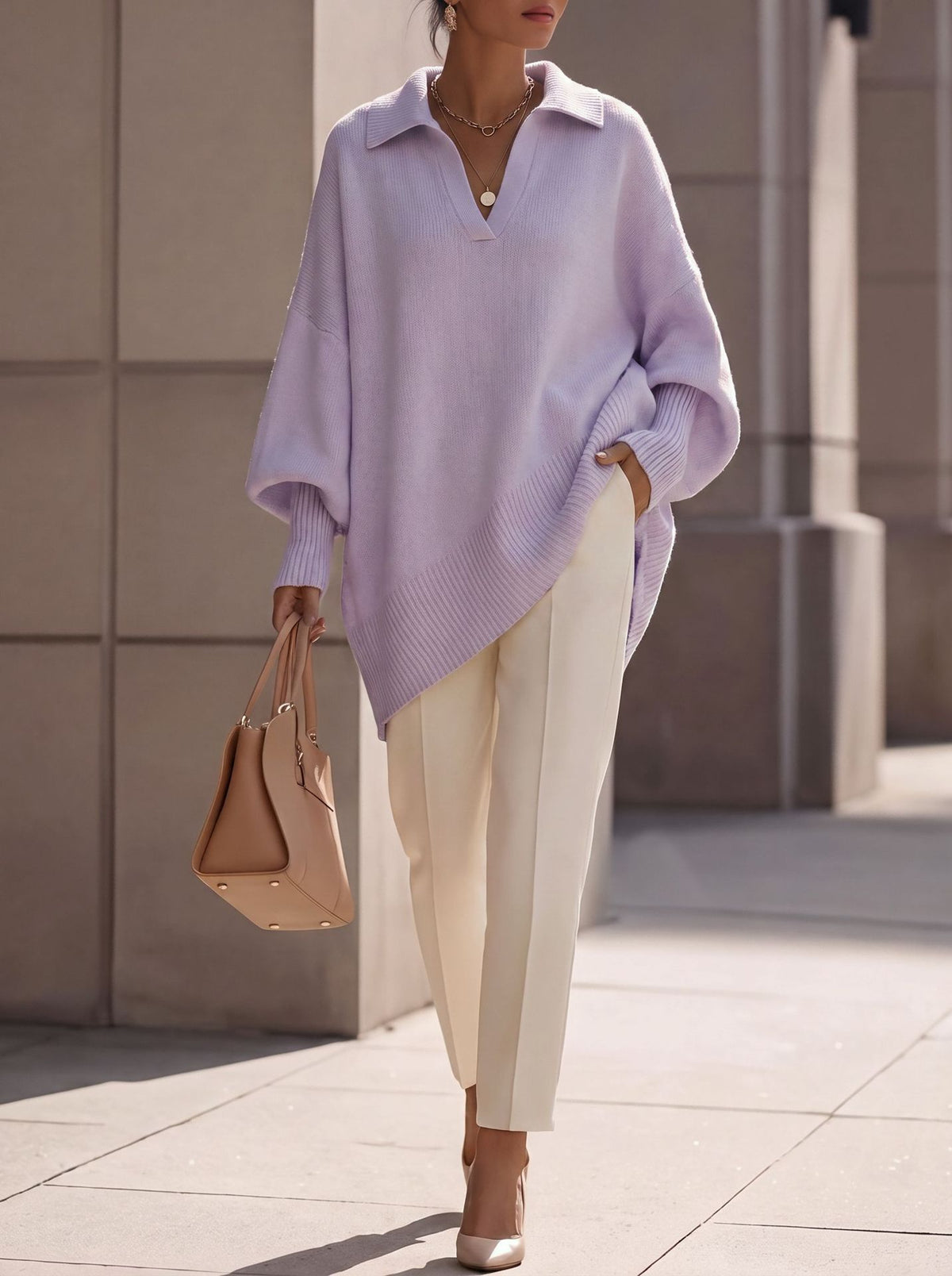 A woman wearing an oversized light purple knit polo sweater, cream-colored trousers, and beige heels, carrying a tan leather handbag while walking outdoors.