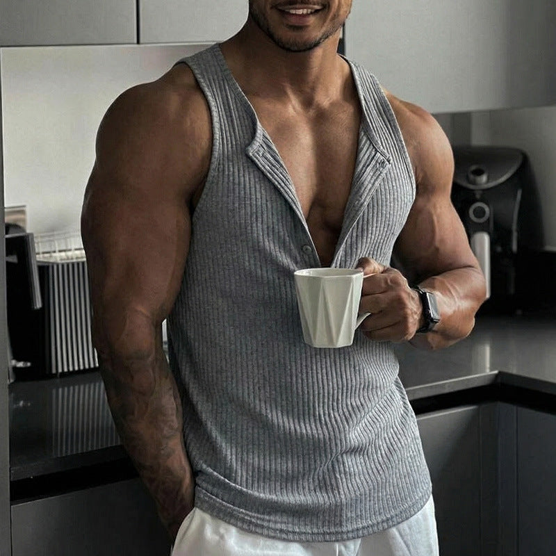 Man in a gray tank top holding a white mug in a kitchen.