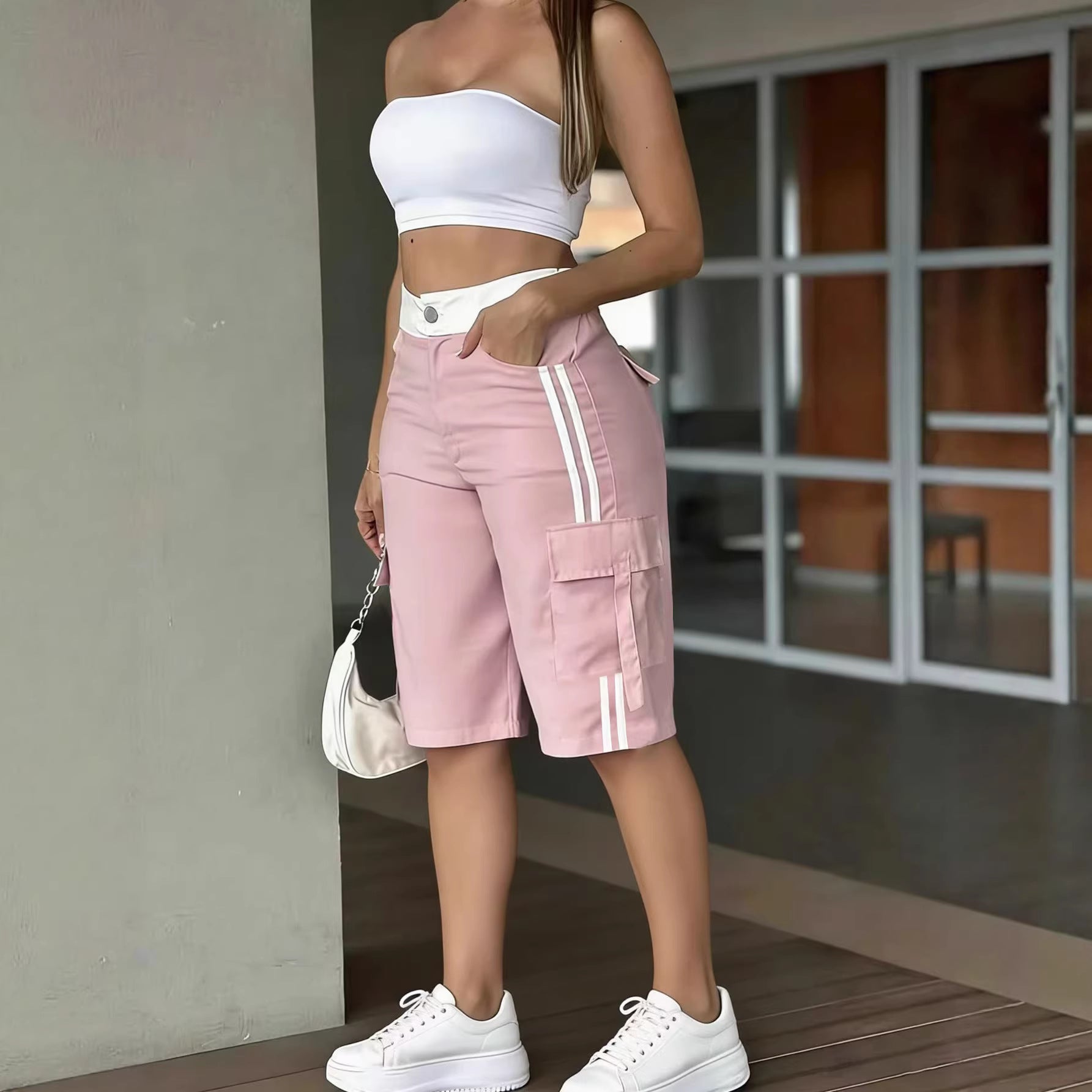 Person wearing a white crop top and pink shorts with white stripes, standing indoors.