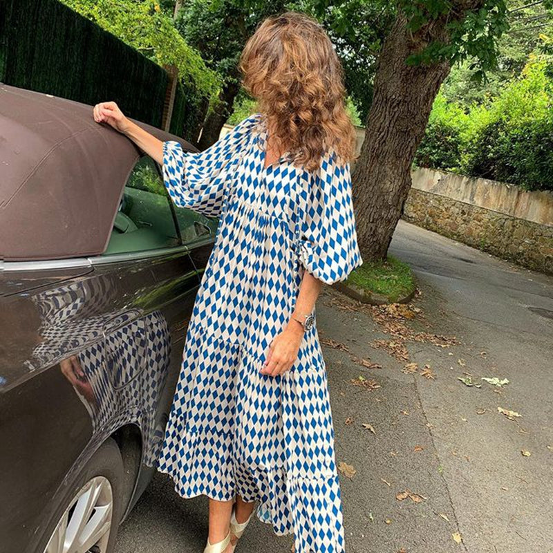 Woman in a blue and white patterned dress opening a car door on a street.