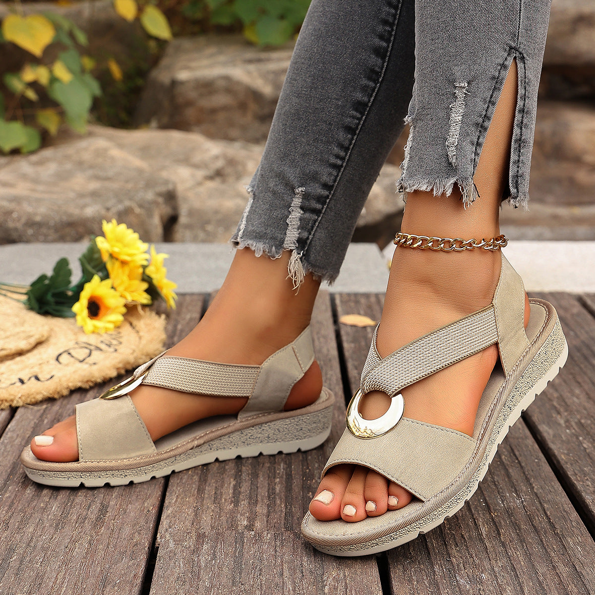 Beige sandals worn with ripped jeans on a wooden surface with flowers in the background