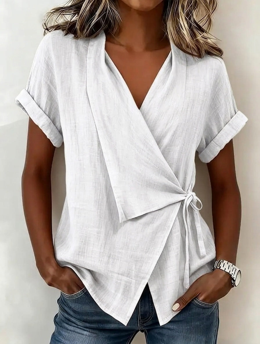 Woman wearing a white wrap-style top with rolled-up sleeves against a neutral background