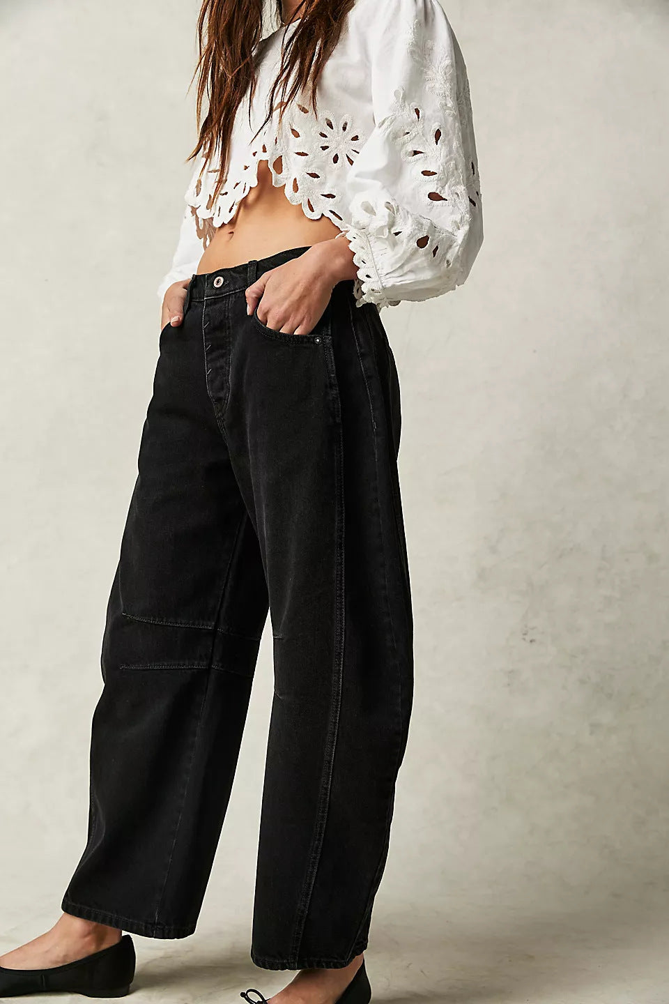 Person wearing a white blouse with floral patterns and black pants on a plain background