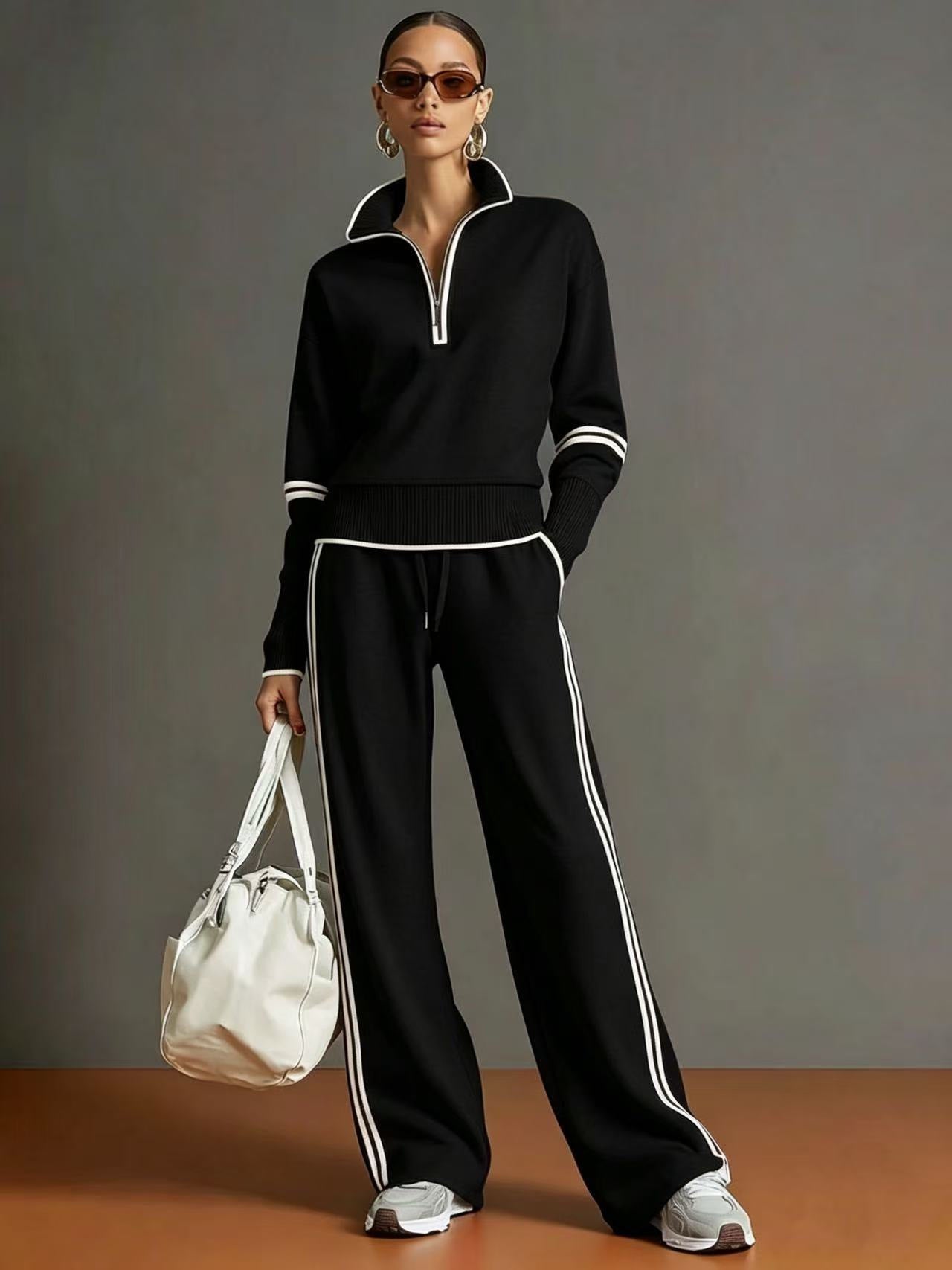 Woman wearing a black tracksuit with white stripes, holding a white bag against a gray background.