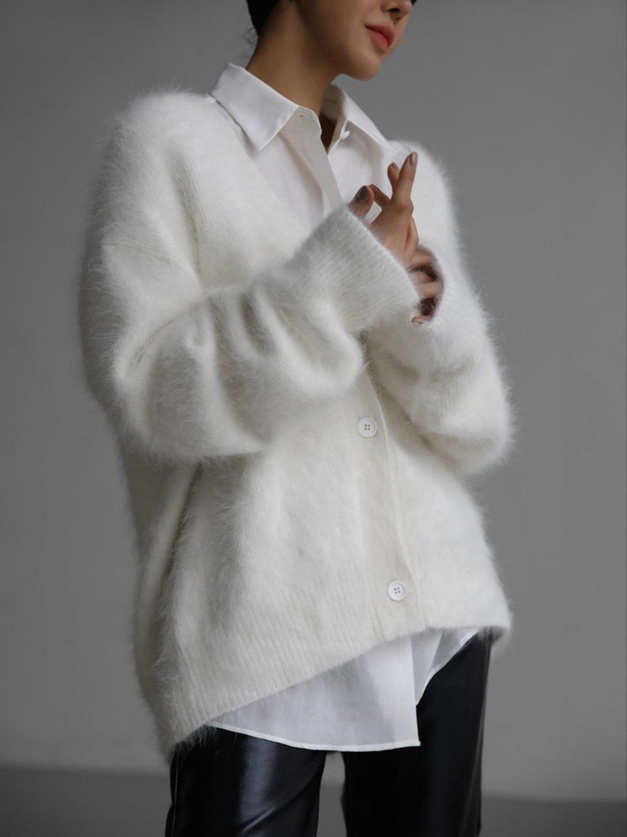 Person wearing a white cardigan over a white shirt with a blurred background