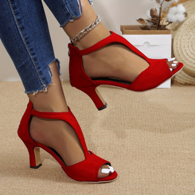 Red high-heeled shoes worn with ripped jeans on a beige carpet.