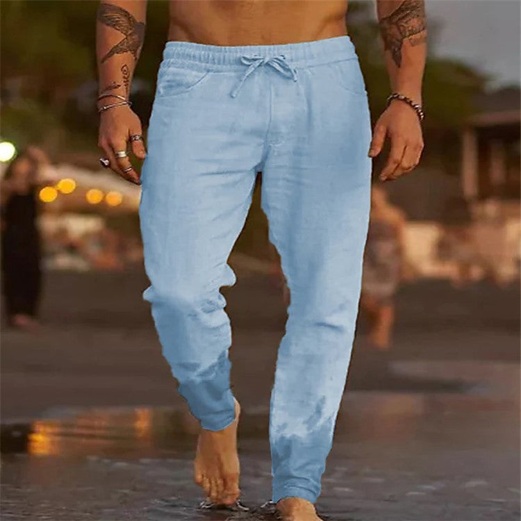 Person wearing light blue jogger pants walking on a beach at sunset.