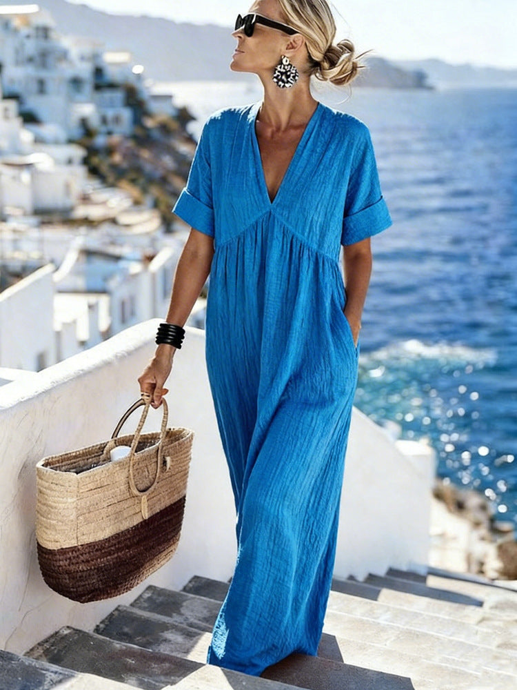Woman in a blue dress standing on a balcony with a scenic view of the ocean and white buildings.