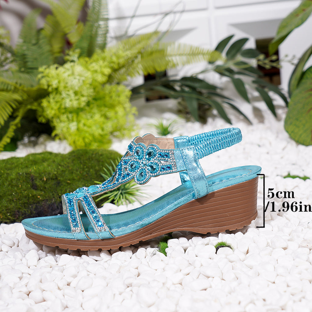 Blue sandal with decorative elements on a white pebble surface with plants in the background