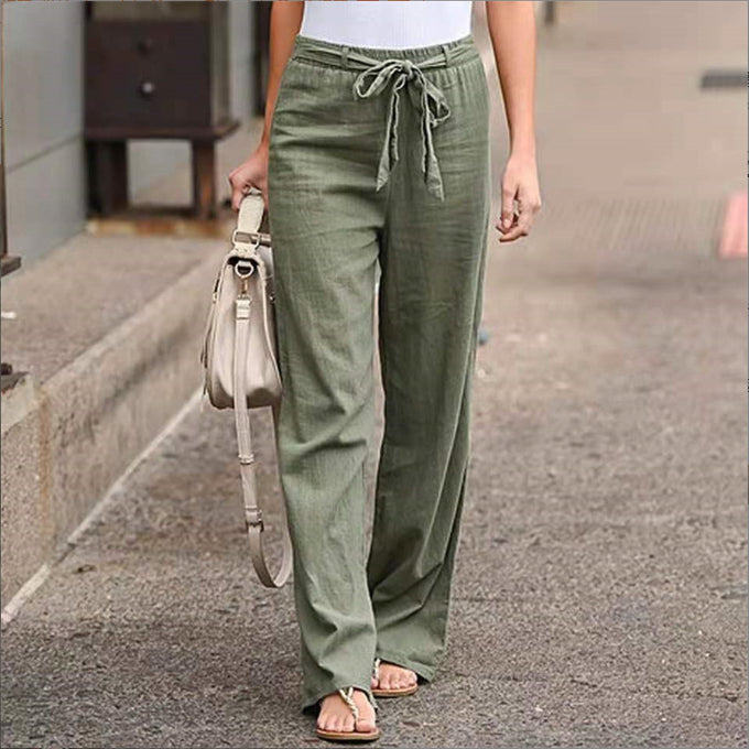 Person wearing green wide-leg pants and a white top, holding a beige handbag on a street.