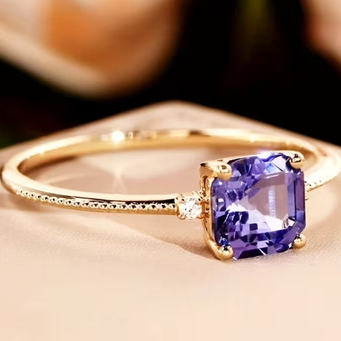 Gold ring with a purple gemstone on a beige surface