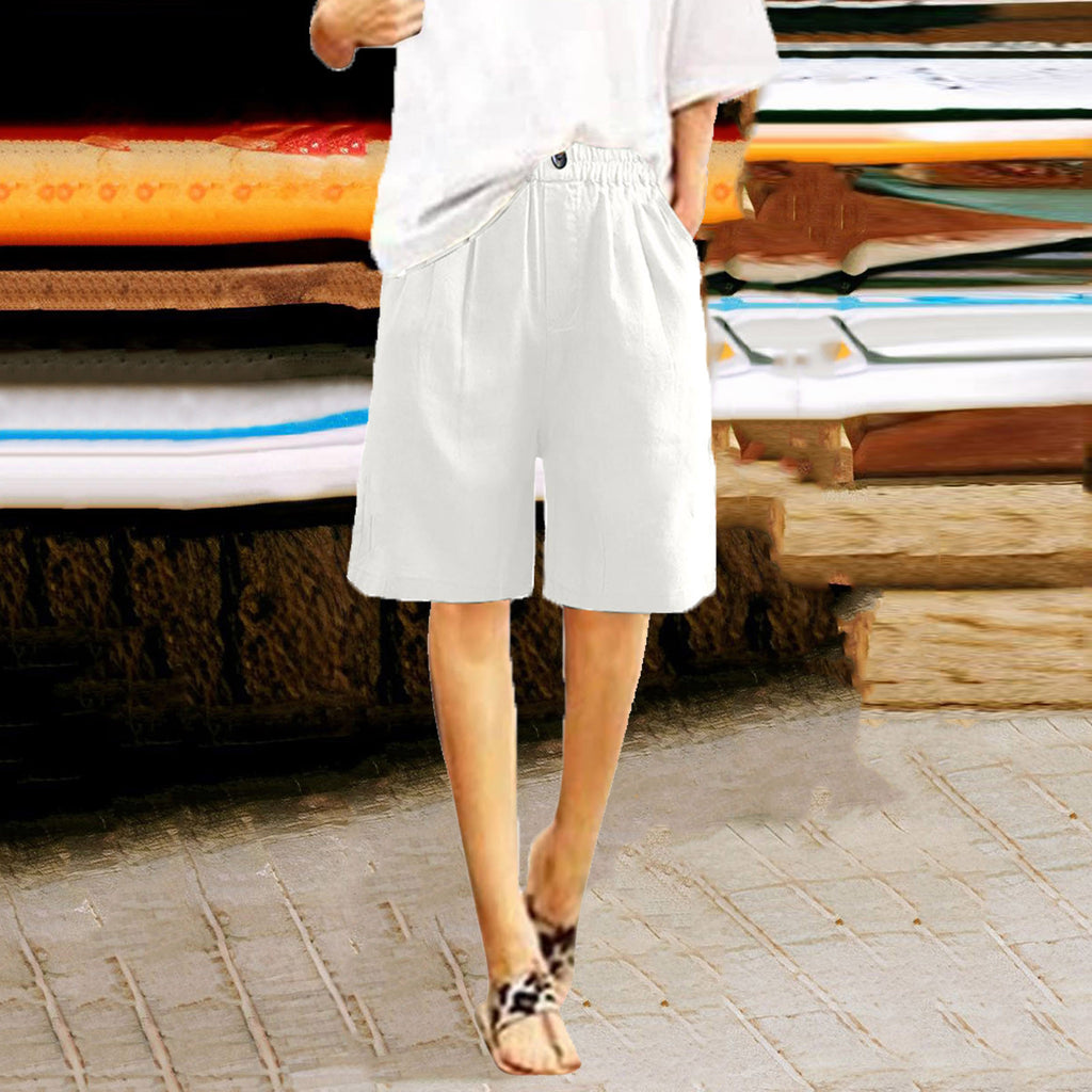 Person wearing white shorts standing in front of stacked surfboards.