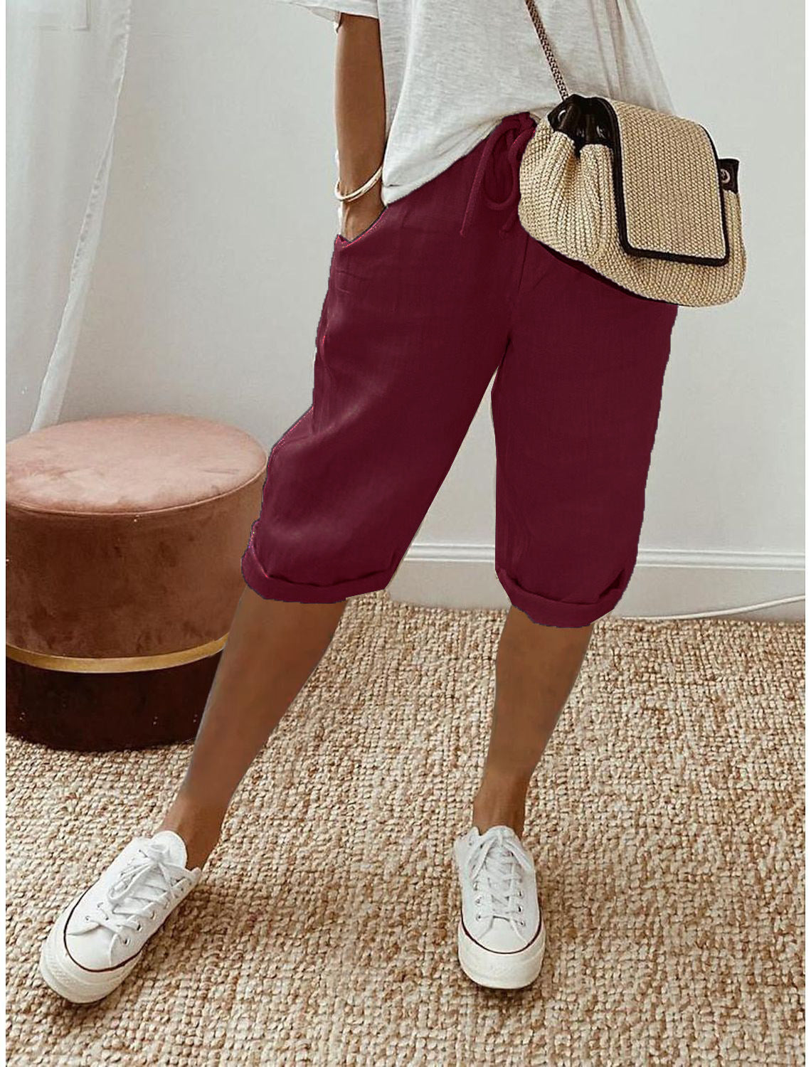 Person wearing maroon shorts, white sneakers, and a straw bag on a carpeted floor.