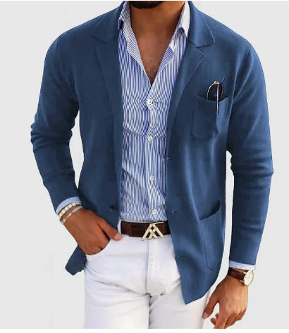 Man wearing a blue blazer over a striped shirt with white pants on a light gray background