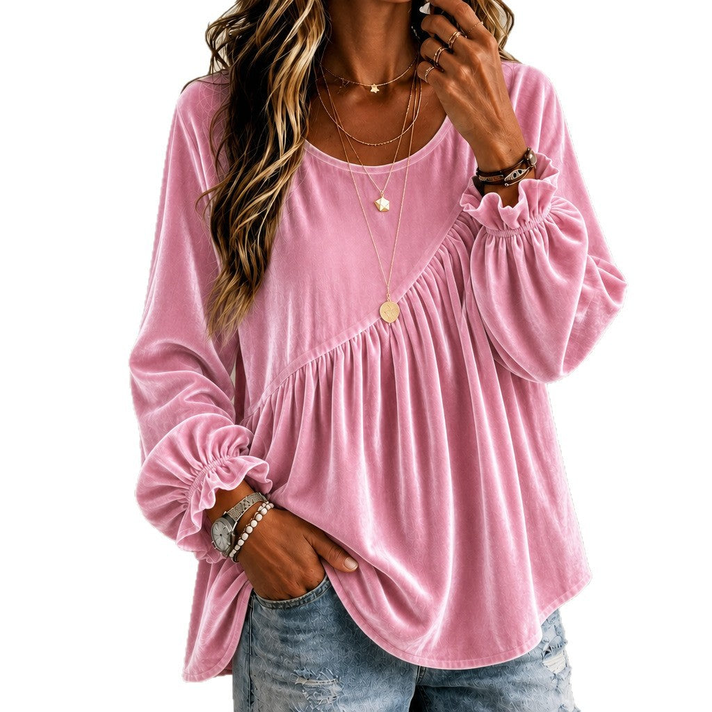 A woman wearing a pink long-sleeve velvet top with ruffled cuffs and a gathered asymmetrical neckline, paired with blue jeans against a plain white background.