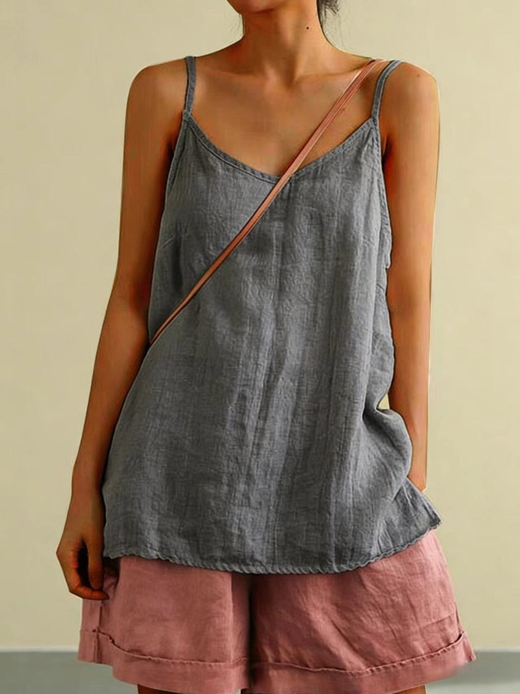 Person wearing a gray tank top and pink shorts with a beige background