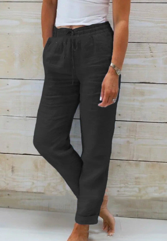 Person wearing black pants and a white top against a wooden background