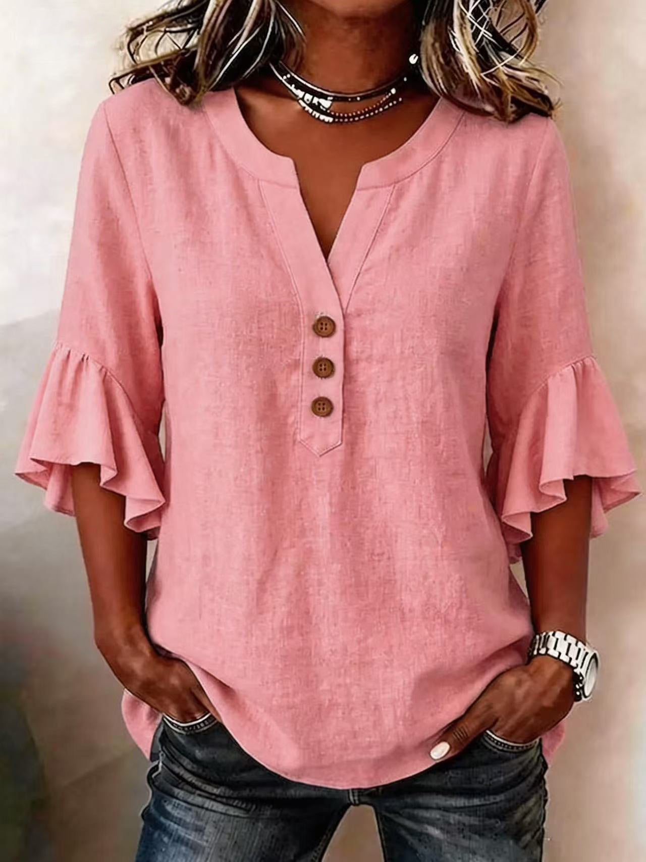 Person wearing a pink blouse with ruffled sleeves and buttons.