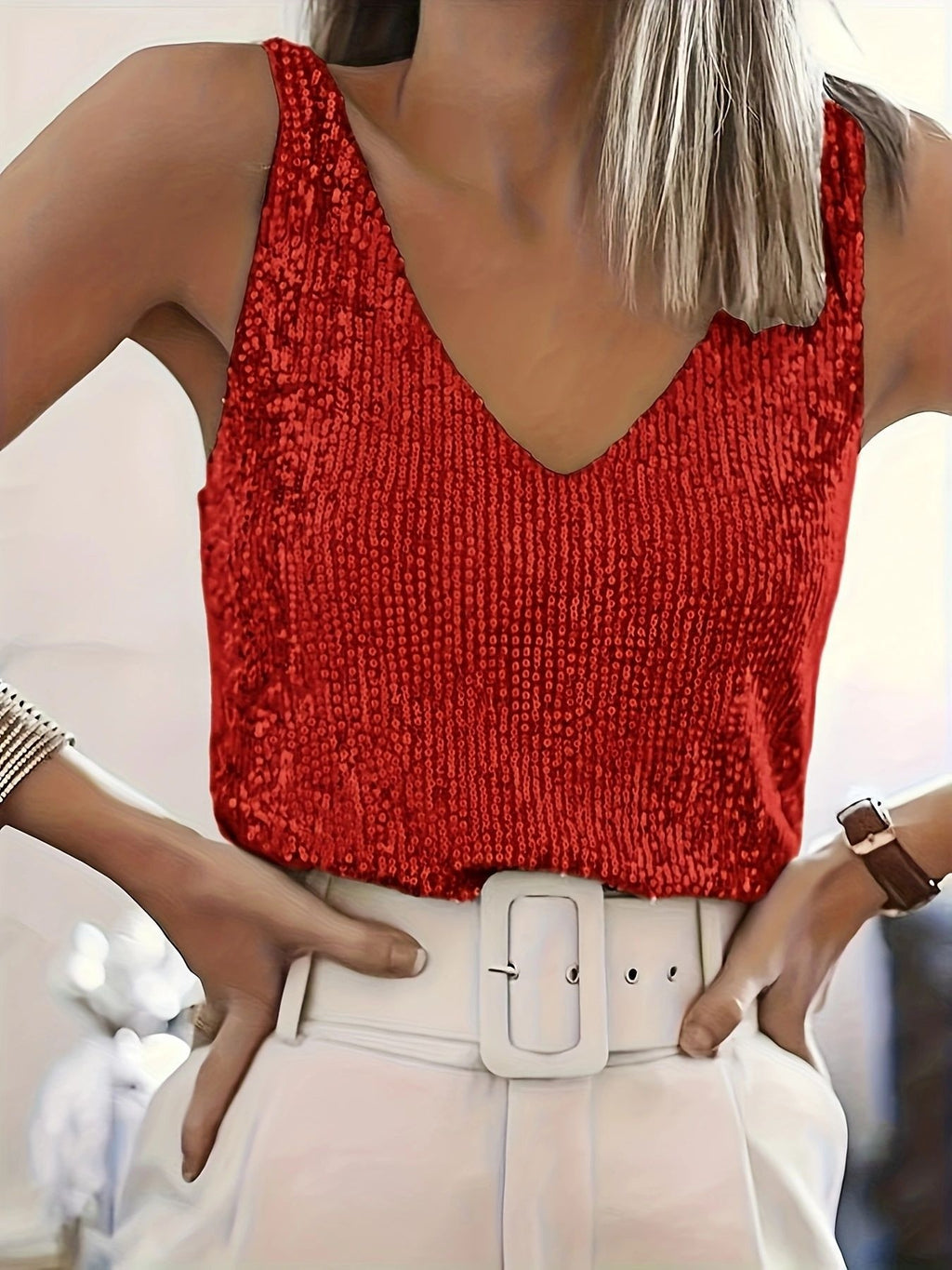 Person wearing a red sequin top and white pants with a blurred background