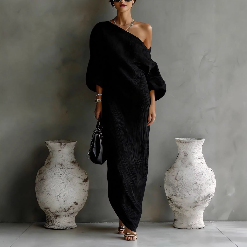 Woman in a black off-shoulder dress standing between two large white vases against a gray wall.