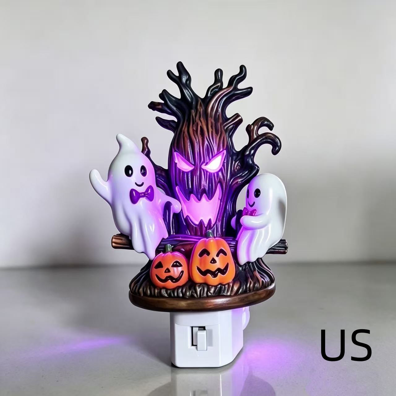 Halloween night light figurine featuring a spooky tree with glowing purple eyes, two white ghosts, and two orange jack-o'-lantern pumpkins on a white plug-in base, shown against a plain light background.